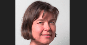 Nærbilde av kvinne som ser i kamera, smiler litt, mørkt, halvlangt hår. Med hvit, nøytral bakgrunn. Avbildet er Anne Spurkland.