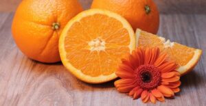 Nærbilde av to hele appelsiner, og en halv, og en oransje blomst. Nøytral bakgrunn.